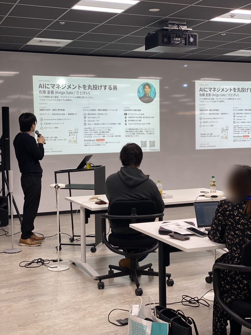 登壇する佐藤圭吾。スクリーンに「AIにマネジメントを丸投げする男」の資料(参加者の顔はぼかし)